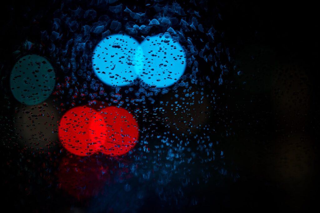 Photo of red and blue lights during rain. Photo by Osman Rana on Unsplash.
