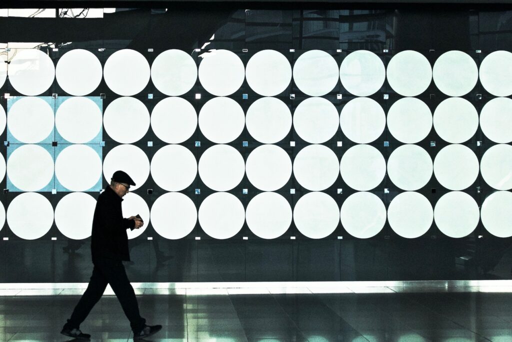 A man dressed in black walking in front of a wall covered with lighted circles.Photo by tam wai on Unsplash.